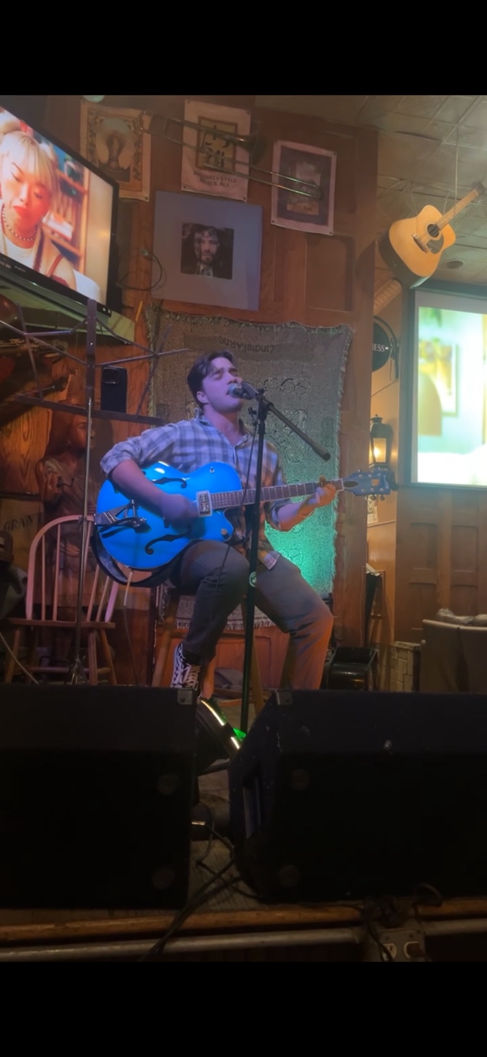 Sullivan McCusker singing and playing a blue guitar on stage